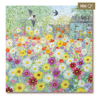 A completed jigsaw puzzle featuring a colorful wildflower meadow with blooming flowers, two flying birds, a bicycle, and a small house. The puzzle is shown at a slight angle with a brown label in the top right corner that reads 'MINI QT'.